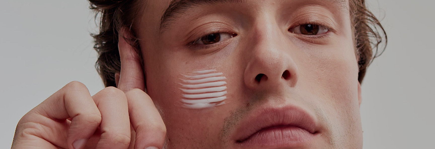 Man applying cream to his face with a neutral background