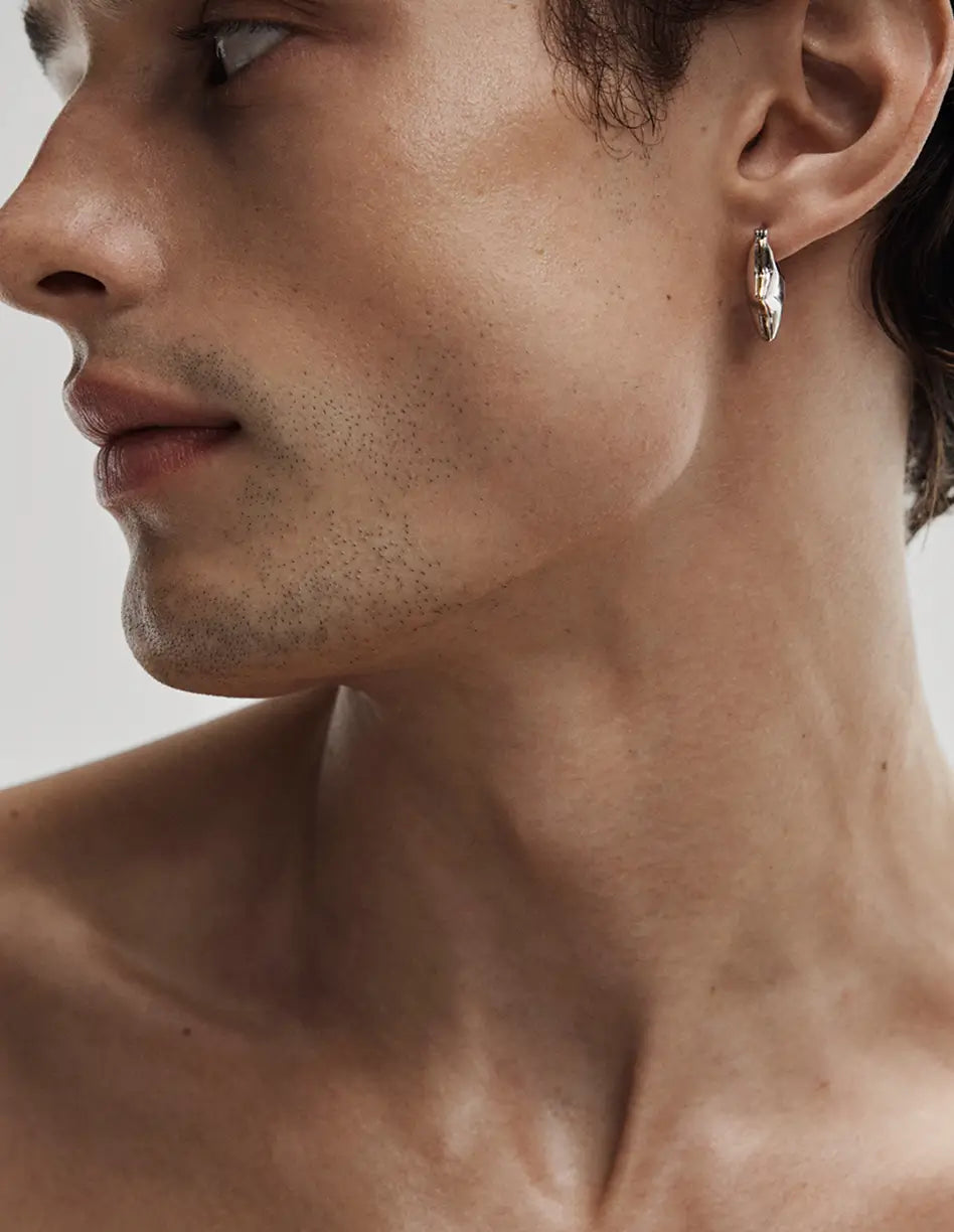 close up of a man wearing a silver hoop earring showing his neck and profile against a neutral background